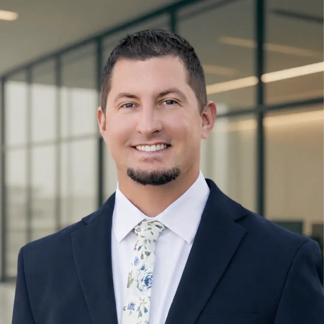 Smiling financial professional in a suit and floral tie, representing Legacy Financial Group, with a modern office background, emphasizing trust and expertise in financial planning.